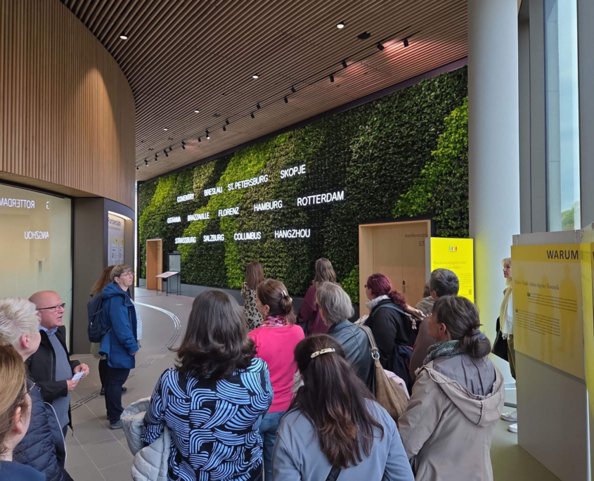 Besucher betrachten die begrünte Wand mit Partnerstädten im Stadtforum Dresden