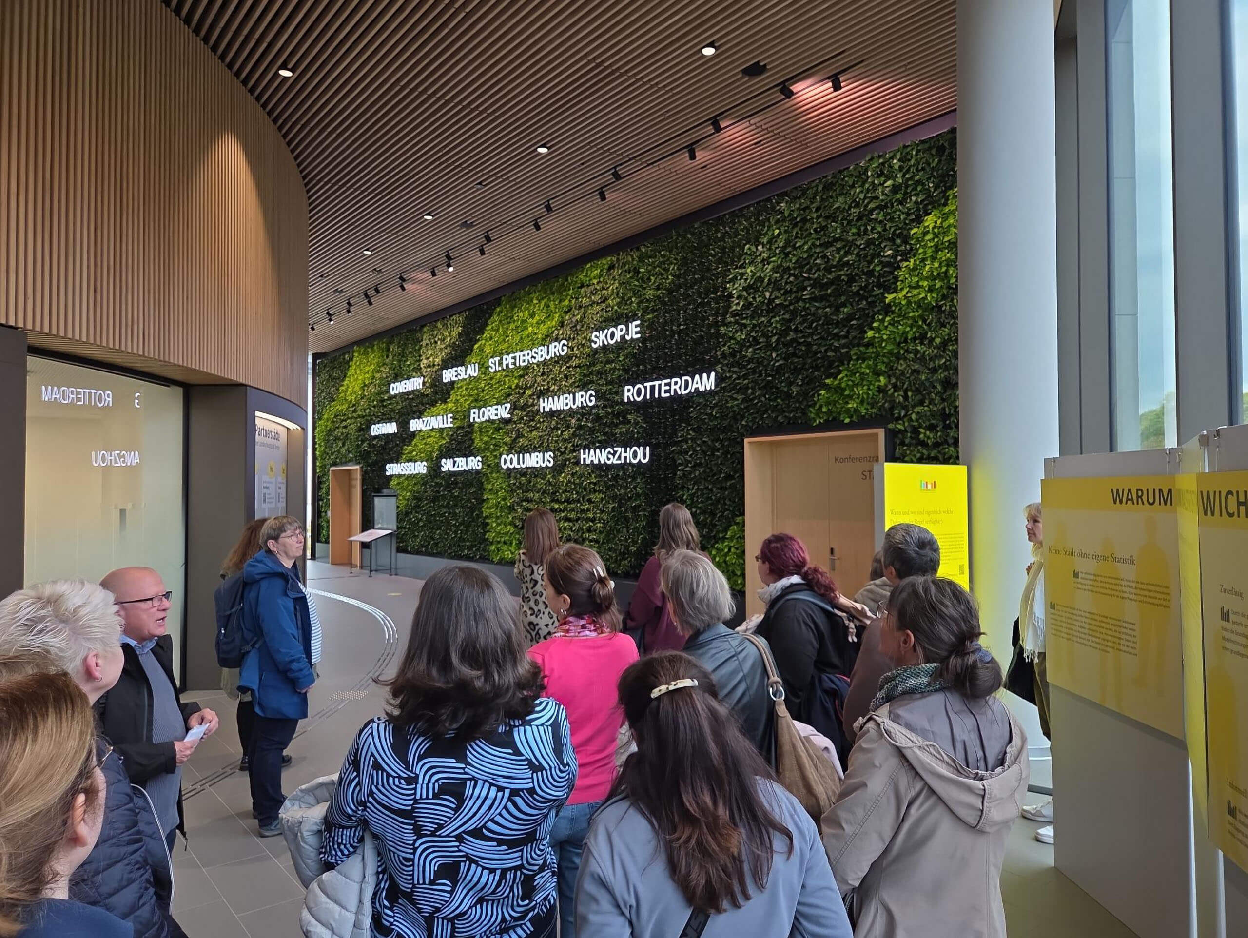 Besucher betrachten die begrünte Wand mit Partnerstädten im Stadtforum Dresden